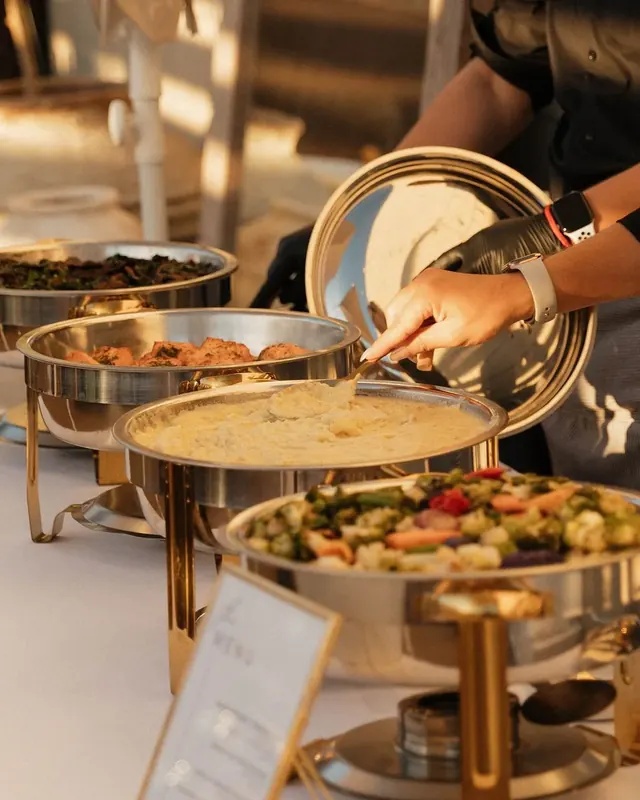 A gloved server lifting the lid of a chafing dish at a catered buffet